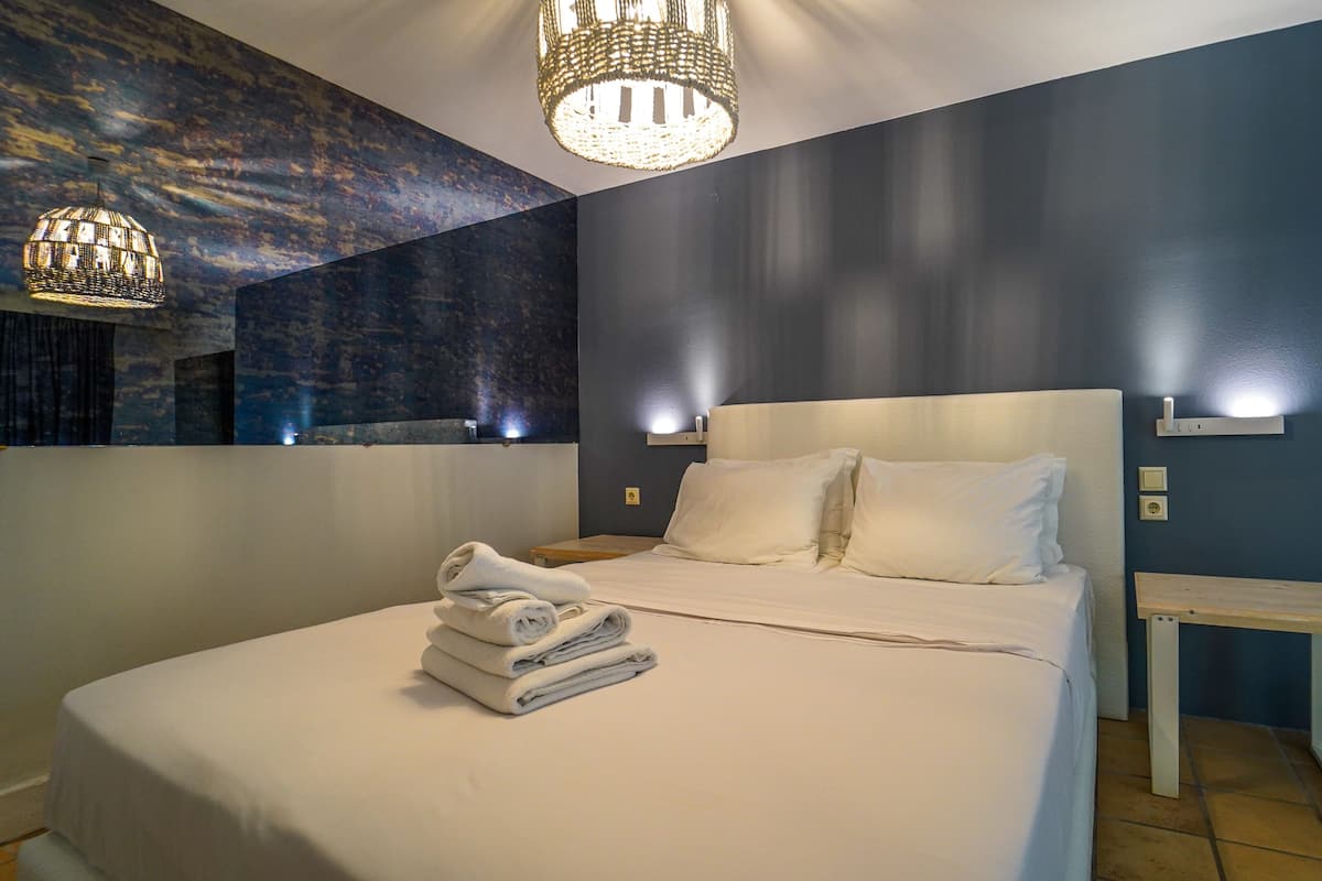 Un lit bien fait, avec du linge de lit et des serviettes blanches, un grand miroir et un lustre moderne.