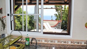 A kitchen with a window overlooking a patio area. - Stonecliff Cottage by Our Madeira (Calheta)
