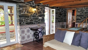 A cozy room with a wicker sofa, a stone wall, and a tiled floor. - Stonecliff Cottage by Our Madeira (Calheta)