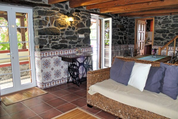 Una habitación acogedora con un sofá de mimbre, una pared de piedra y suelo de baldosas.