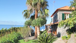 A stone building with a red-tiled roof, a palm tree, and a view of the sea. - Stonecliff Cottage by Our Madeira (Calheta)
