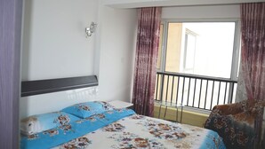 Une chambre d’hôtel comprenant un lit, une table de chevet, une lampe fixée au mur, un balcon avec une rambarde et des rideaux.