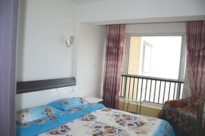 Habitación de hotel con cama, mesita de noche, lámpara de pared, balcón con barandilla y cortinas.