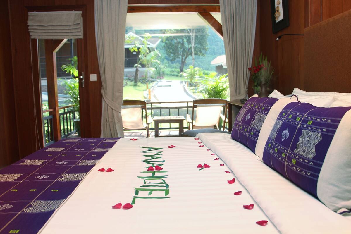 A hotel room with a bed, a balcony, and a view of greenery.