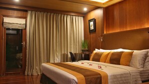 A hotel room with a bed, curtains, a small table with a plant, and a framed picture on the wall.