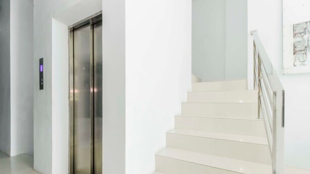 Een moderne lift en een trap met een metalen leuning.