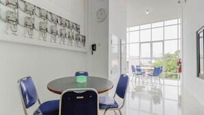 Een vergaderruimte met een ronde tafel, blauwe stoelen, een klok en een raam met uitzicht op de omgeving.