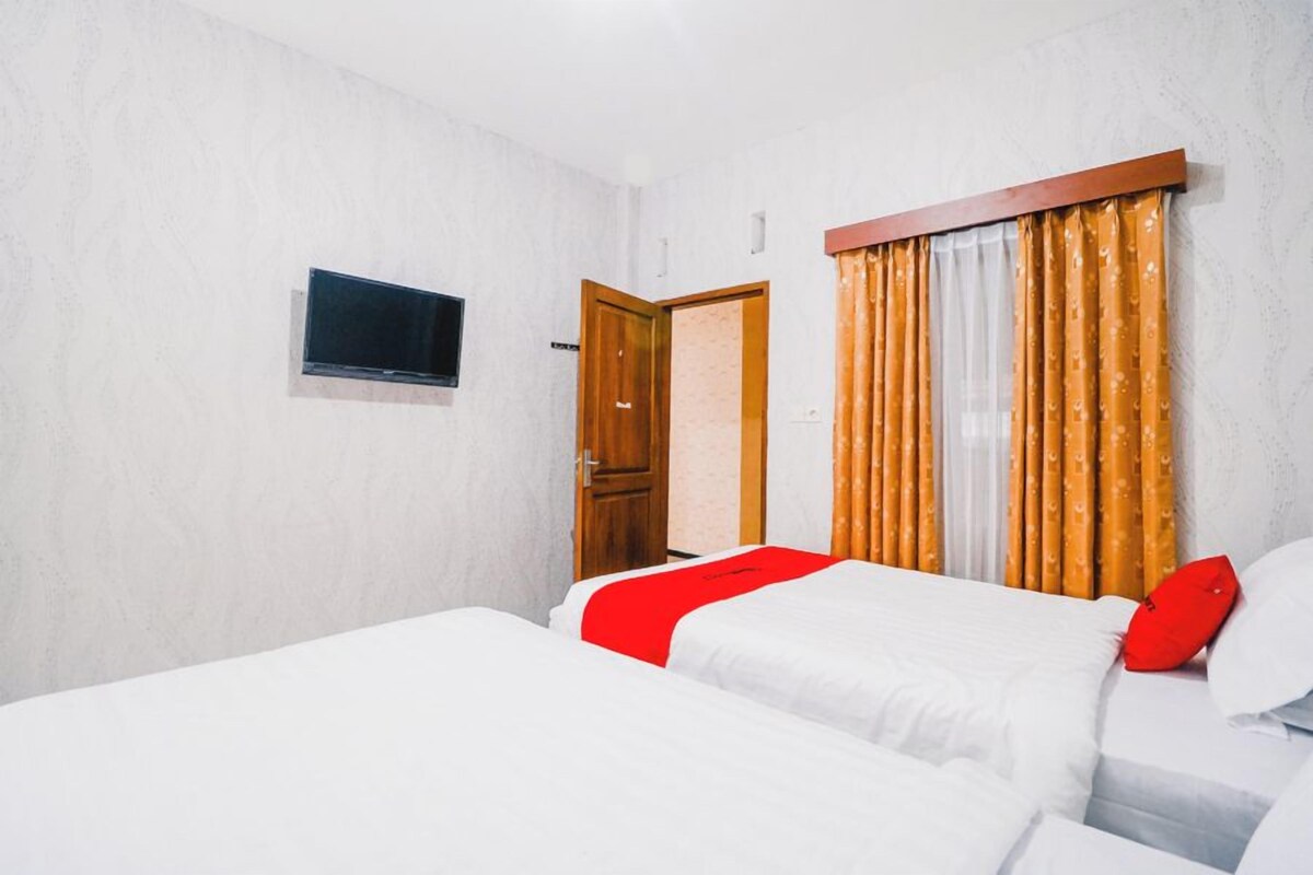 A hotel room with two beds, a television, a wooden door, and a window with curtains.