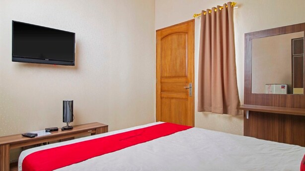 Une chambre d’hôtel avec un lit, un téléviseur fixé au mur, une porte en bois et un miroir au-dessus du lit.