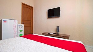 Une chambre d’hôtel avec un lit, un téléviseur fixé au mur, une porte en bois et une petite table avec une lampe.