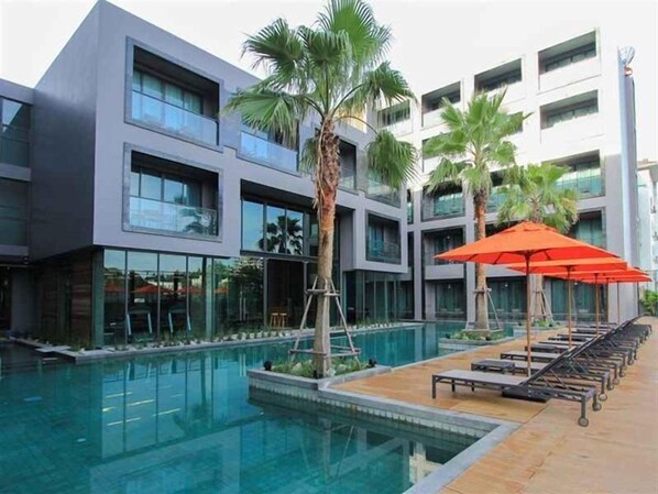 A modern building with a pool area, including lounge chairs and umbrellas. - Sugar Marina Resort  Surf  Kata (Karon)