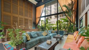 A spacious indoor area with a large window, wooden panel walls, and various seating arrangements including sofas and a coffee table. - Sugar Marina Resort  Surf  Kata (Karon)