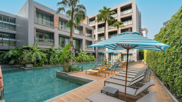 A modern hotel with a swimming pool, lounge chairs, and a large umbrella. - Sugar Marina Resort  Surf  Kata (Karon)