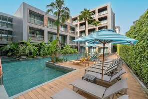 Un hotel moderno con piscina, sillones de descanso y una gran sombrilla.