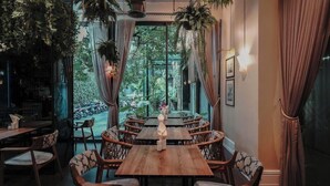 A restaurant with a wooden table and wicker chairs, surrounded by curtains and plants. - Sugar Marina Resort  Surf  Kata (Karon)