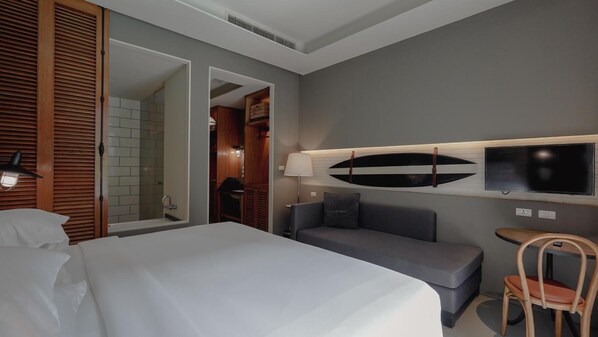 Habitación de hotel con cama, sofá, televisión montada en la pared y una silla de madera.