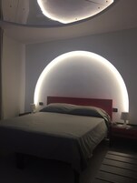 Quarto moderno com luminária de teto curva, cama com cabeceira vermelha e mesas de cabeceira com luminárias.