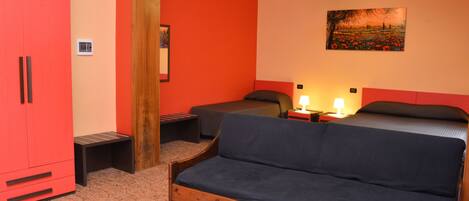 Una habitación con un armario rojo grande, un sofá de madera, una cama con dos almohadas, una mesita con una lámpara y un cuadro en la pared.