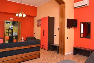 Quarto com cama, escrivaninha, cadeira, guarda-roupa, televisão e ar condicionado.