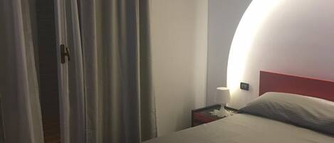 A bedroom with a bed, a nightstand, a lamp, and a door with curtains.