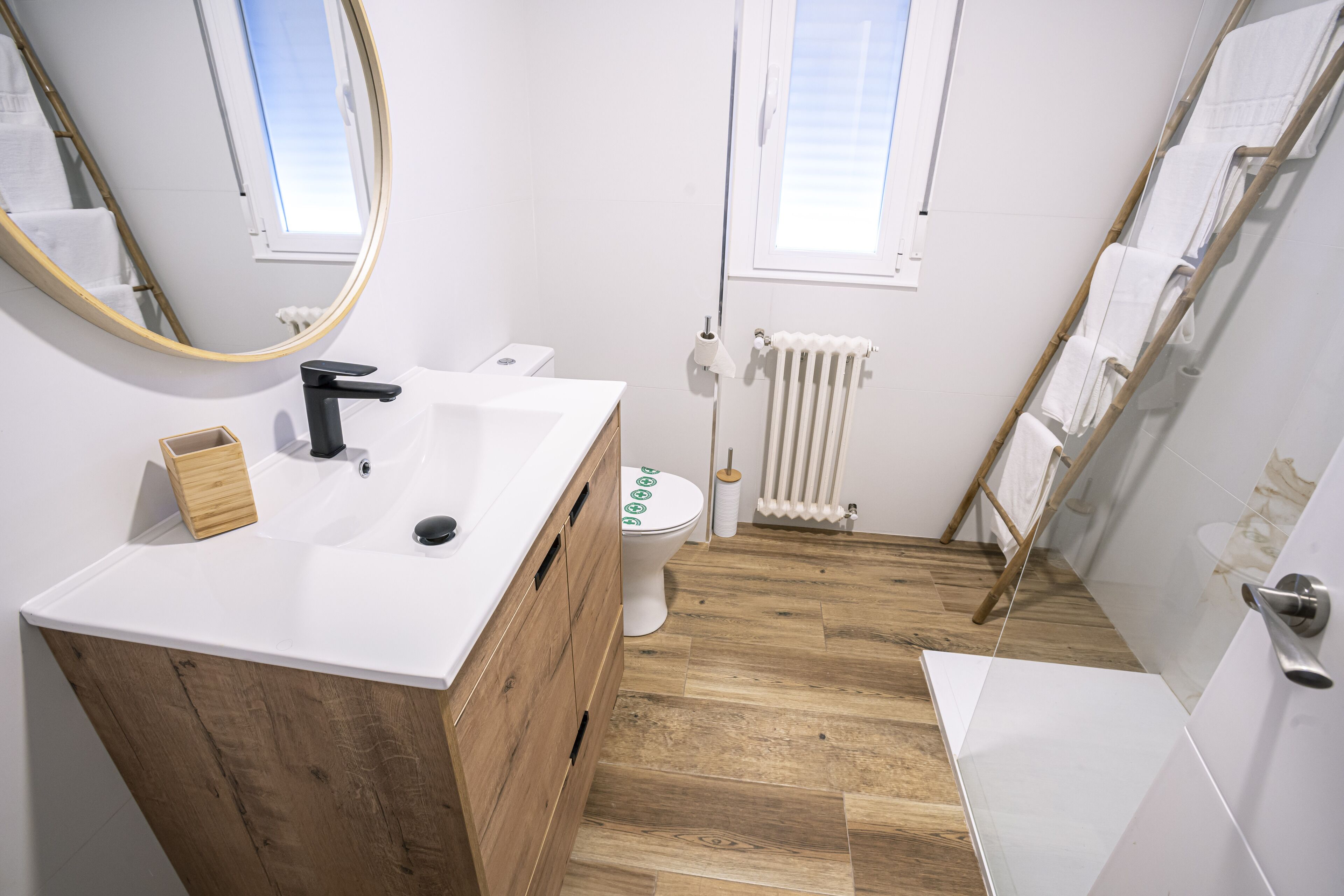 Un bagno moderno con un mobile bagno in legno, un lavandino bianco, un water e una zona doccia.