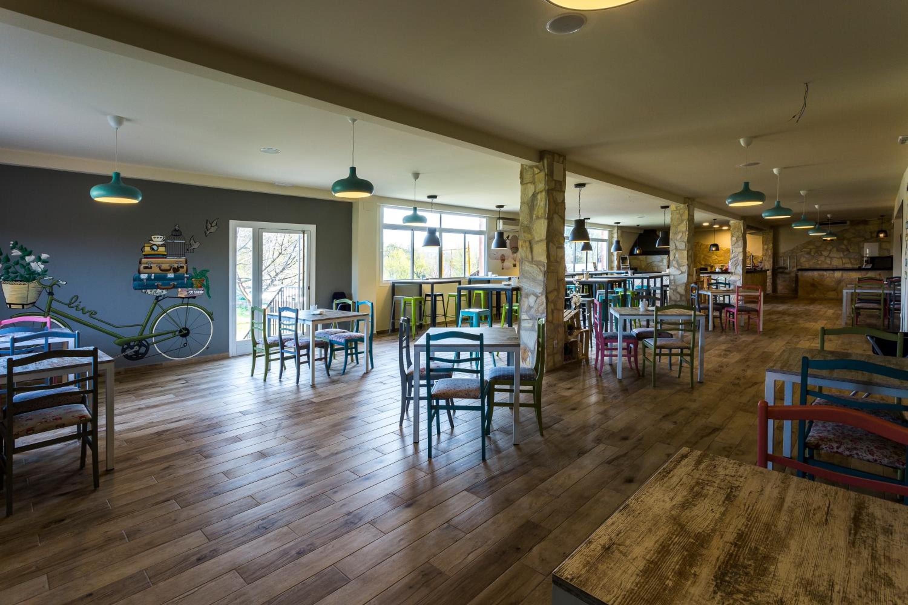 A spacious indoor area with wooden flooring, multiple tables and chairs, and hanging pendant lights.