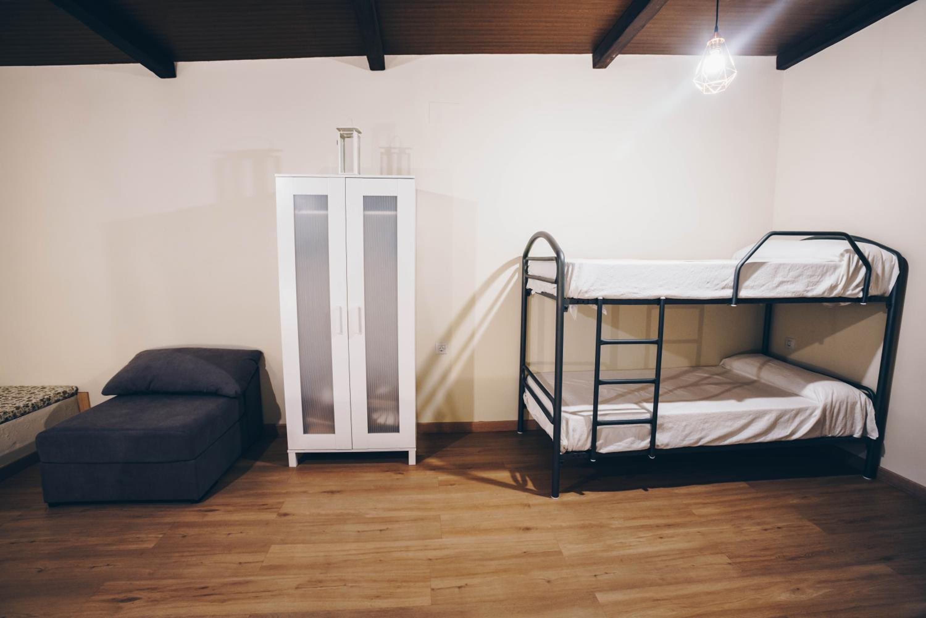 A bunk bed with a ladder, a small sofa, and a cabinet in a room with wooden flooring and a sloped ceiling.