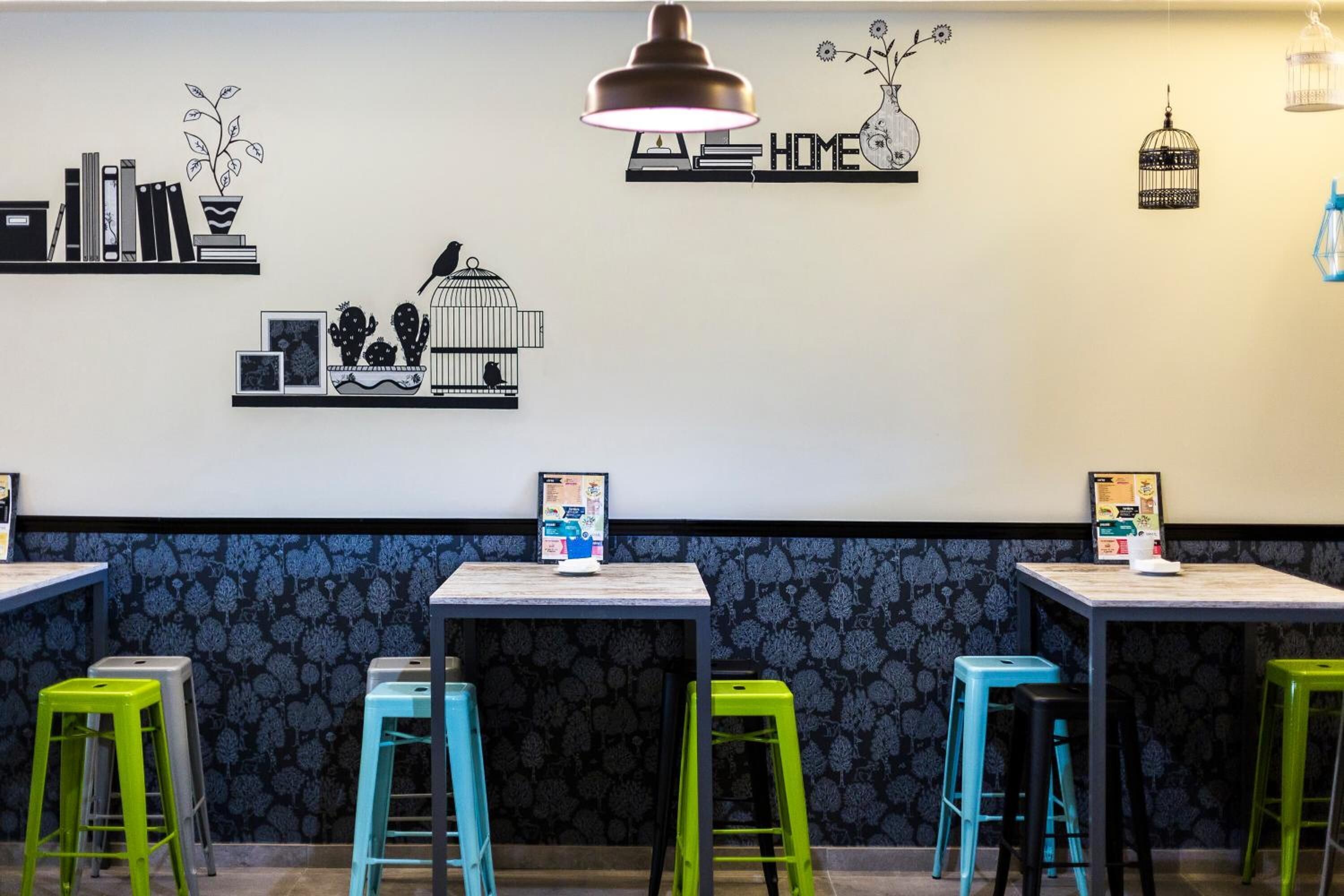 A restaurant interior with a black and white wall decor, a hanging lamp, and colorful stools.