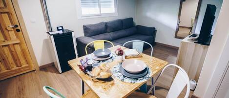 Un espacio habitable compacto con comedor, sofá, kitchenette pequeña y un espejo.