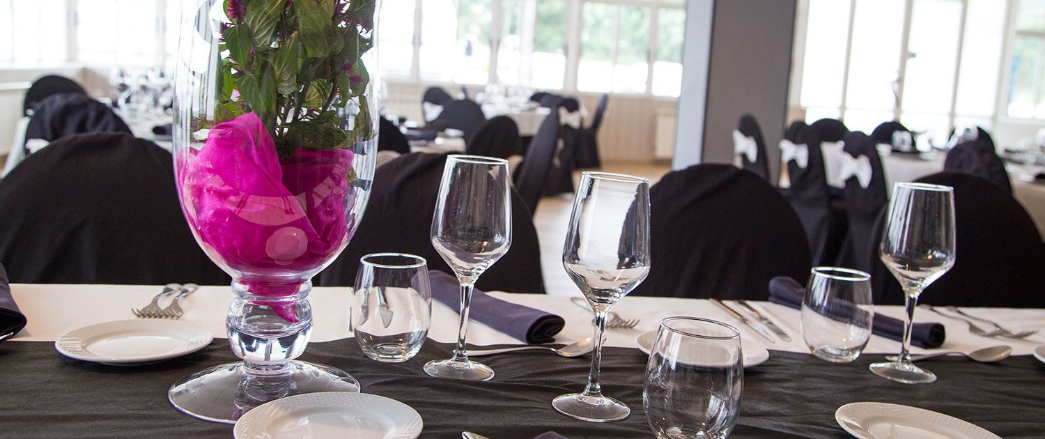 A dining table set with clear glassware and a vase with pink flowers.