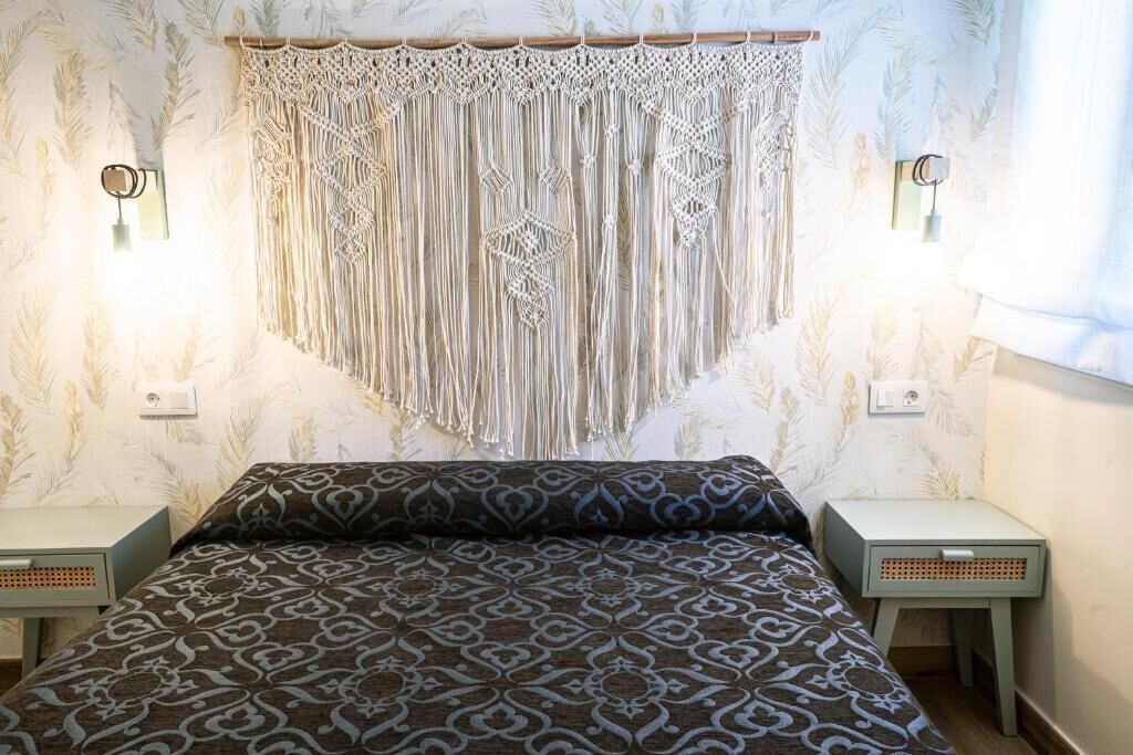 Une chambre à coucher avec une couvre-lit à motifs, une décoration murale en macramé et deux lampes de chevet.