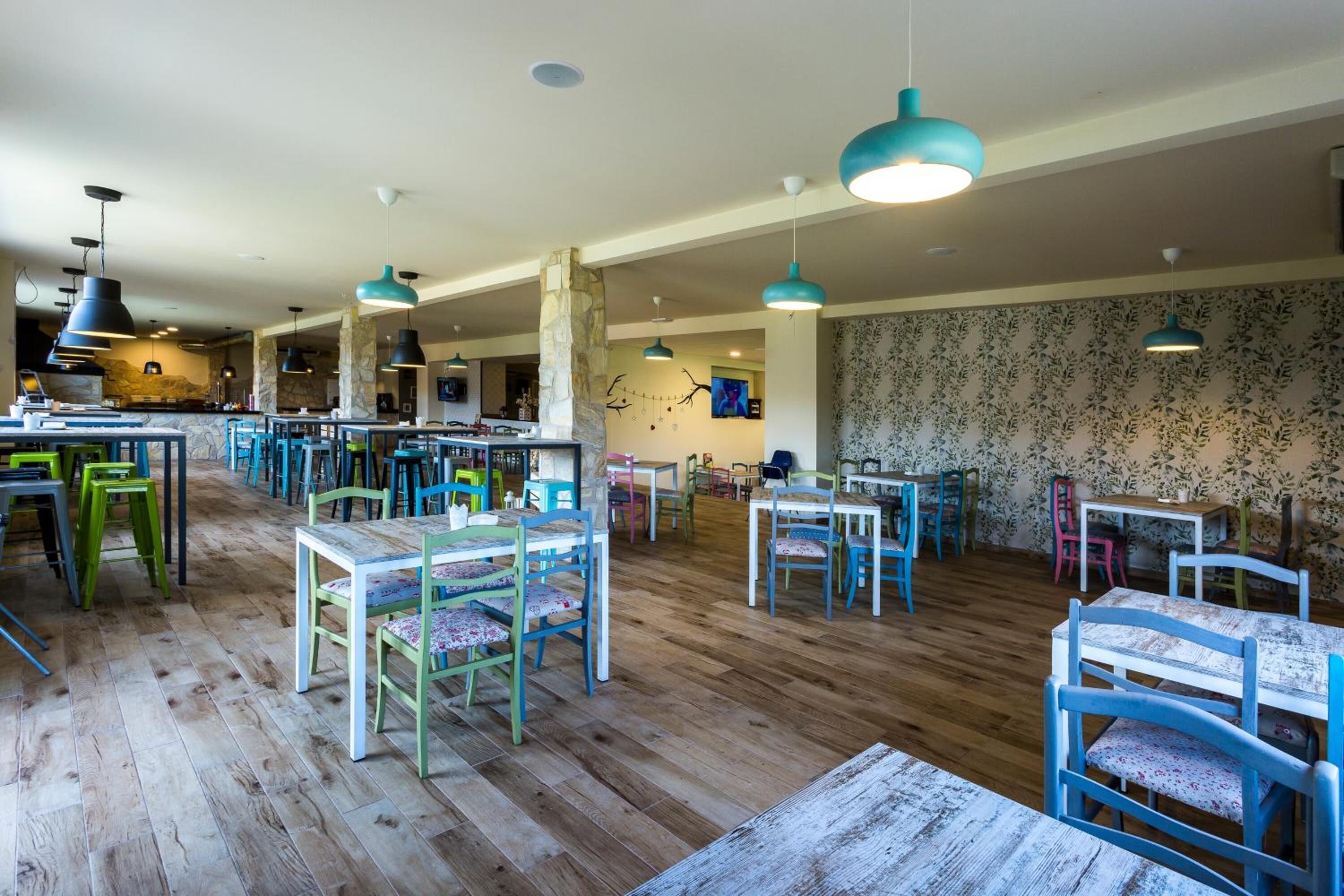 A spacious dining area with wooden floors, colorful chairs, and pendant lighting.