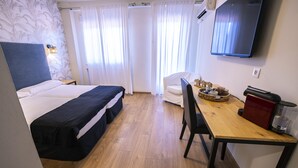 Habitación de hotel con cama, escritorio, silla, televisor y ventana con cortinas.