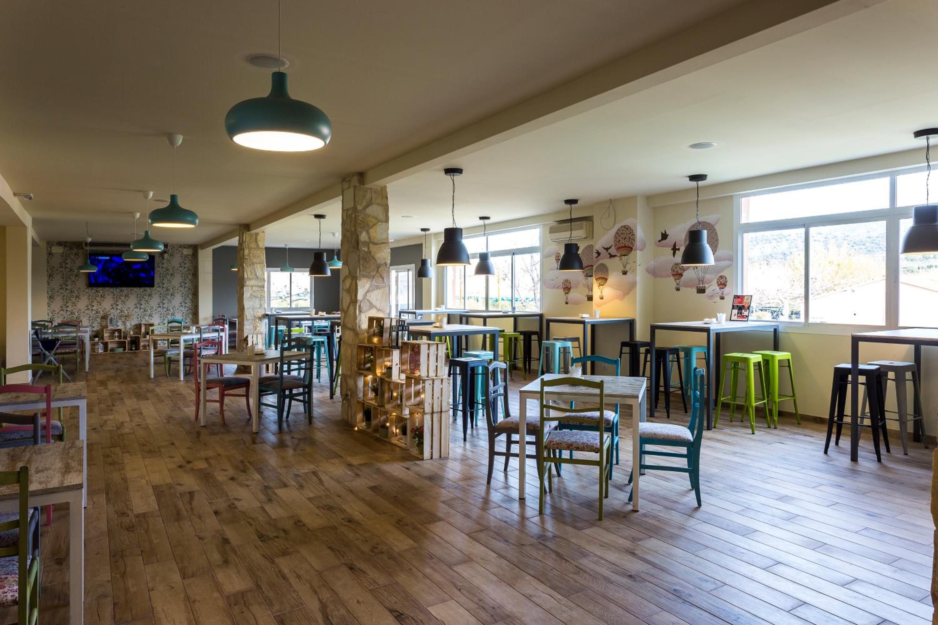 A spacious restaurant with wooden floors, multiple tables and chairs, and pendant lighting.