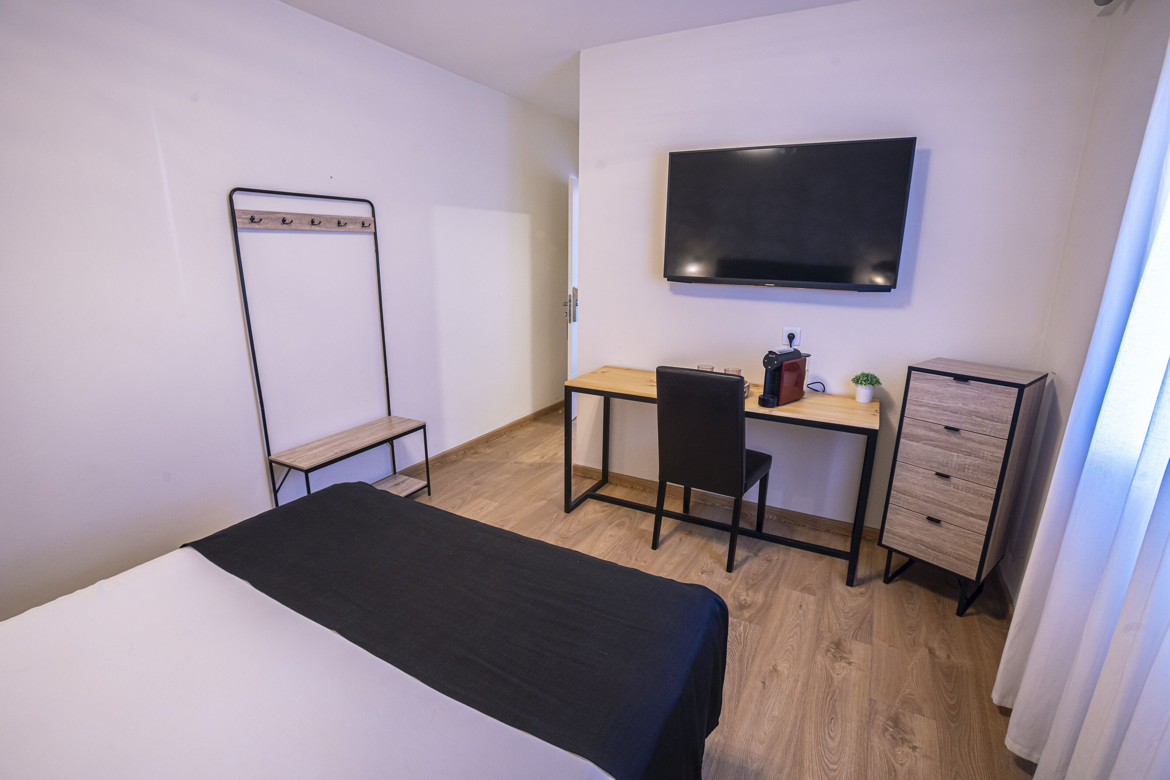 Ein Hotelzimmer mit Bett, Schreibtisch, Stuhl, Fernseher und Kleiderschrank.