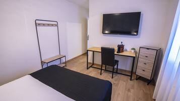 Una habitación de hotel con cama, escritorio, silla, televisor y armario.