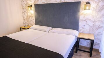 Un lit double avec une tête de lit grise, deux tables de chevet et une petite table de nuit avec une lampe.