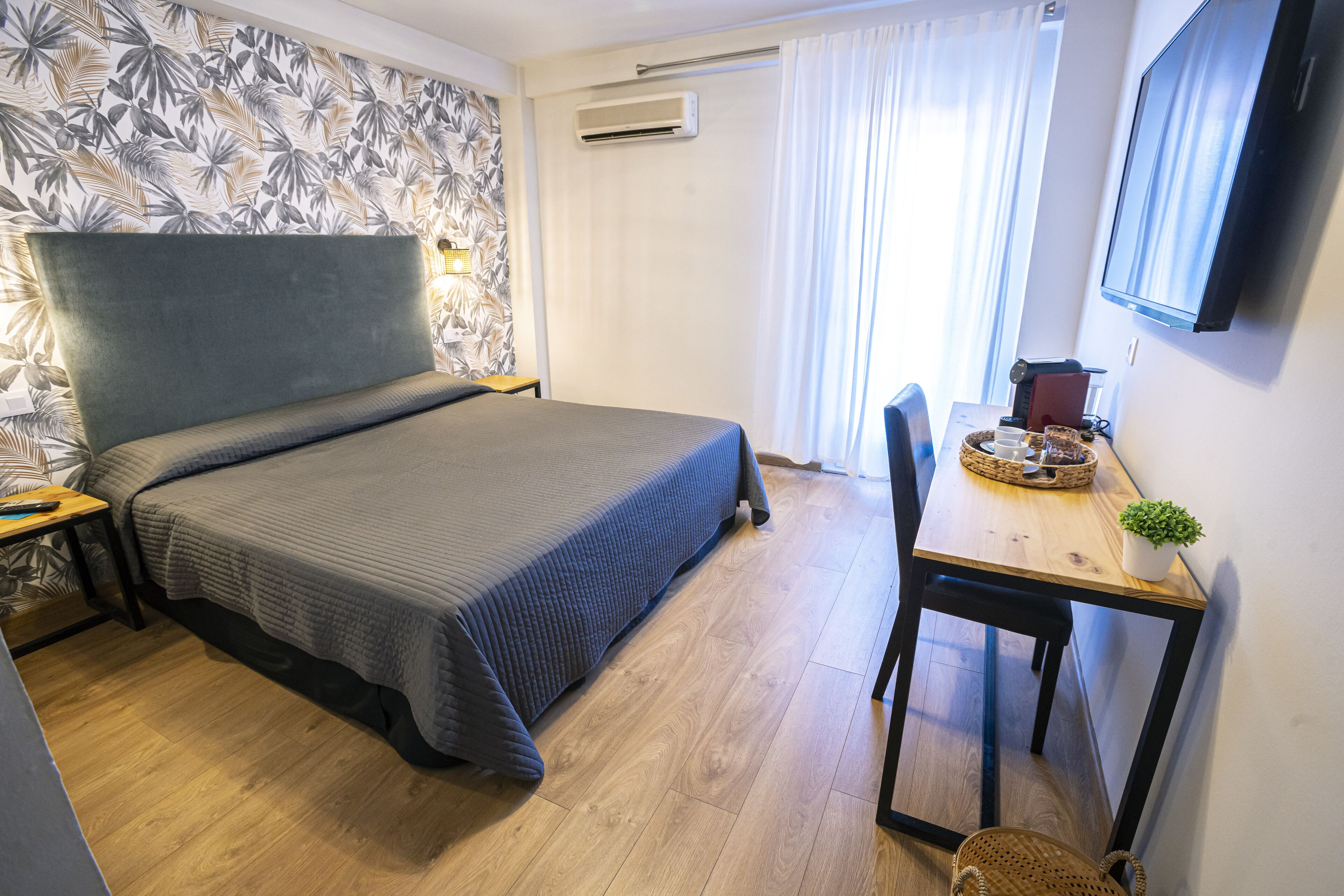 Una habitación de hotel con cama, escritorio con silla, televisor y ventana con cortinas.