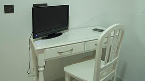 Un escritorio blanco con una computadora, una silla y un espejo en la pared.