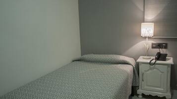 Une petite chambre avec un lit simple, une table de chevet avec une lampe et un tableau de distribution électrique fixé au mur.