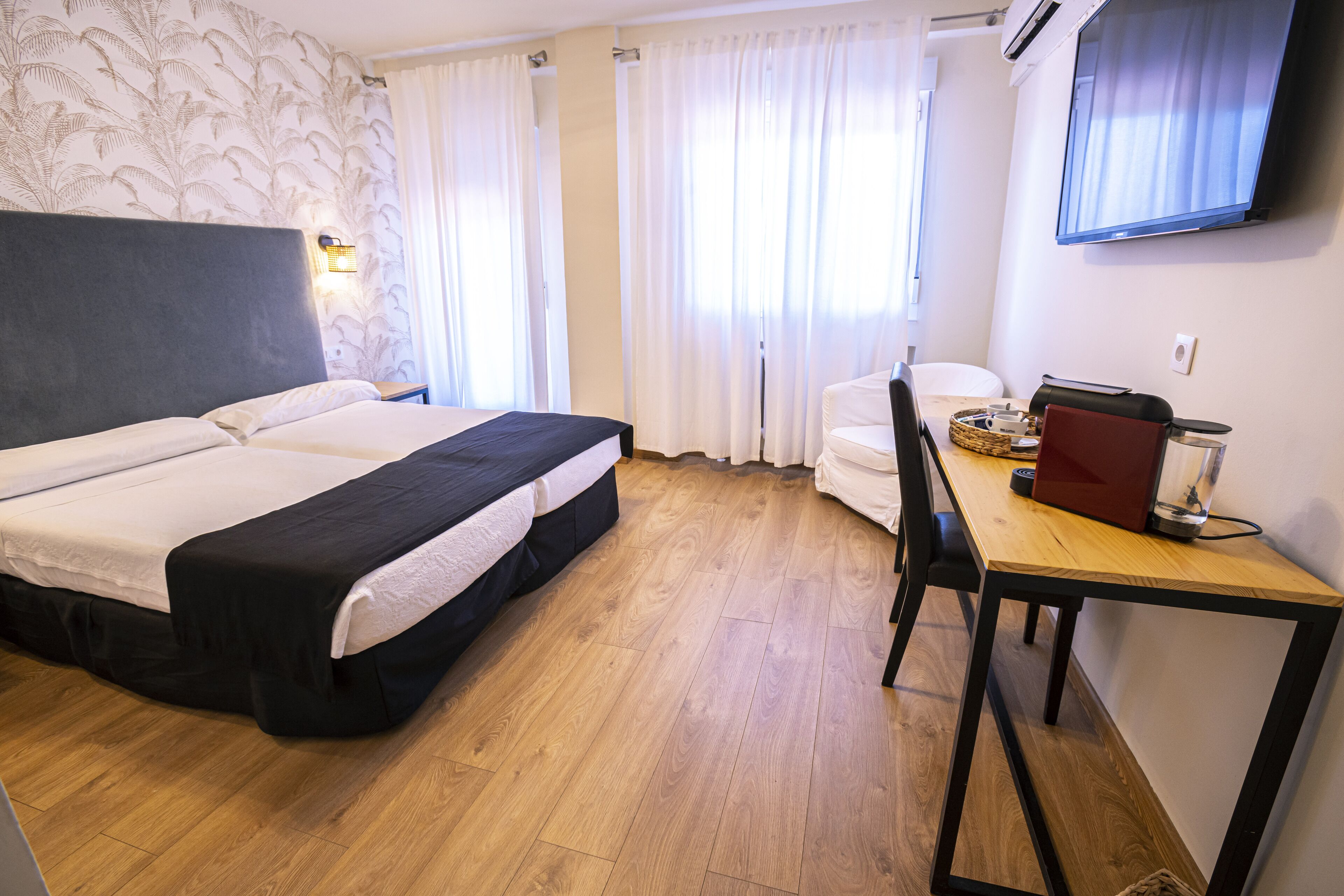 A hotel room with a bed, a desk, a chair, a television, and a window with curtains.