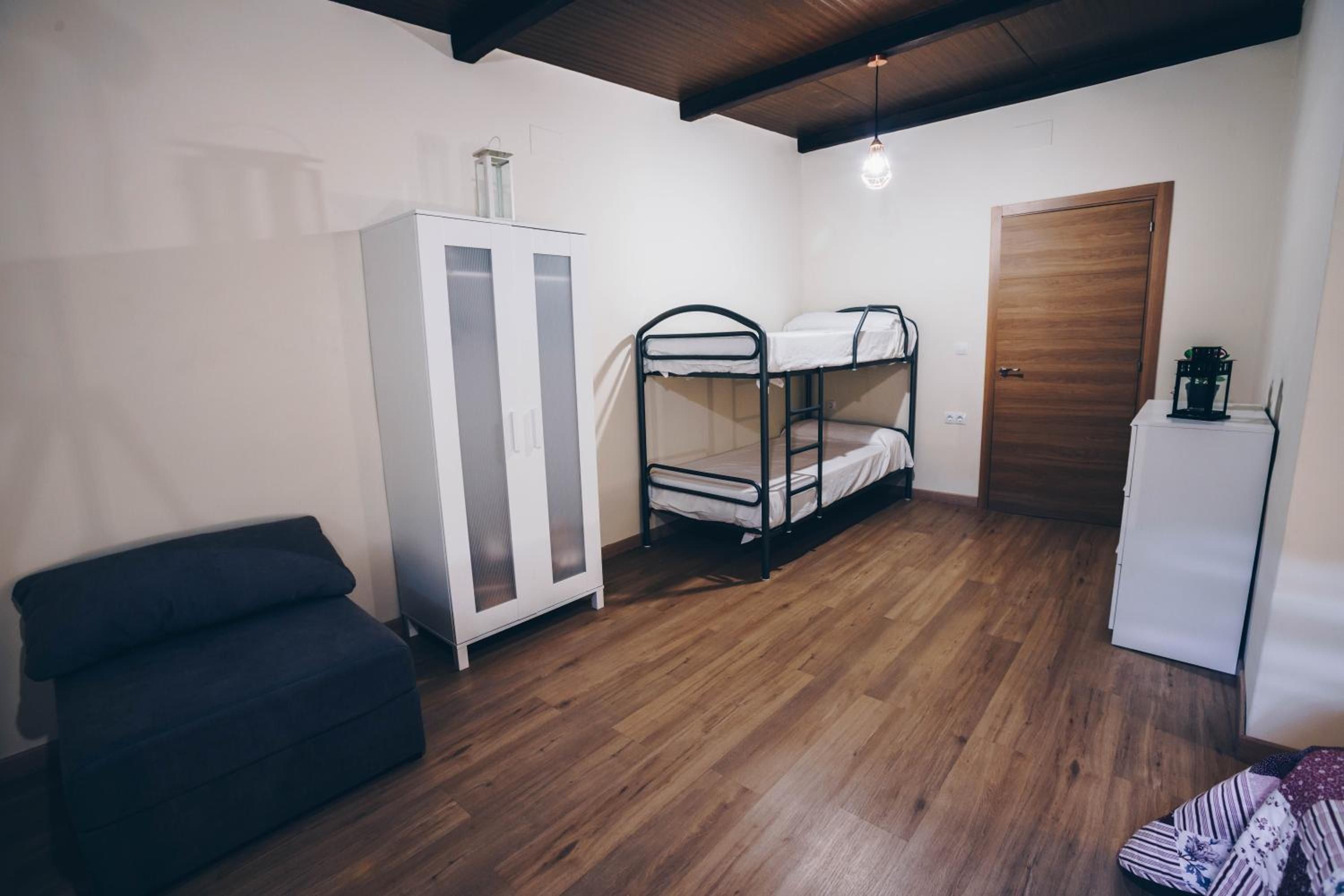 Una habitación con literas, un armario, una mesita con una planta y una puerta.