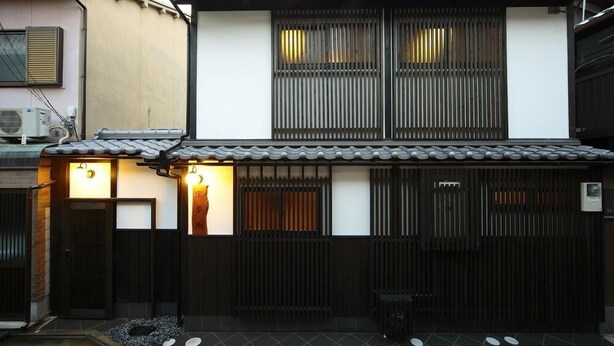 A traditional Japanese house with a tiled roof, sliding doors, and a small garden area with stepping stones. - Kyoyumean (Kyoto)