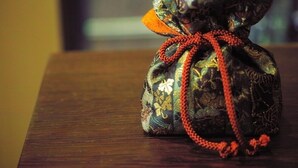 A small, intricately designed bag with a floral pattern and an orange ribbon, placed on a wooden surface. - Kyoyumean (Kyoto)