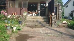 A stone staircase leading to a wooden door, surrounded by potted plants and a stone wall. - Le Café Cerisier (Myoko)