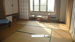 A Japanese-style room with tatami flooring, a low table, two chairs, a window with curtains, and a traditional sliding door. - Le Café Cerisier (Myoko)