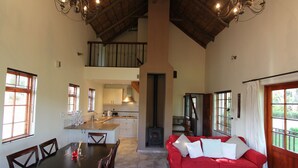 Amplia sala de estar con un sofá rojo, una mesa de comedor de madera y sillas. Se ve una cocina al fondo, con una estufa de leña en el centro.
