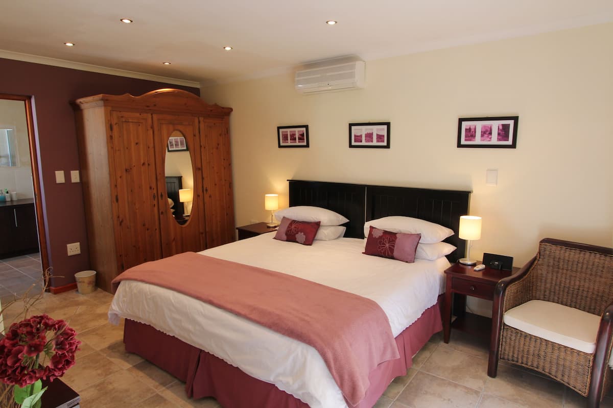 A hotel room with a large bed, a wooden wardrobe, a wicker chair, and framed pictures on the wall.