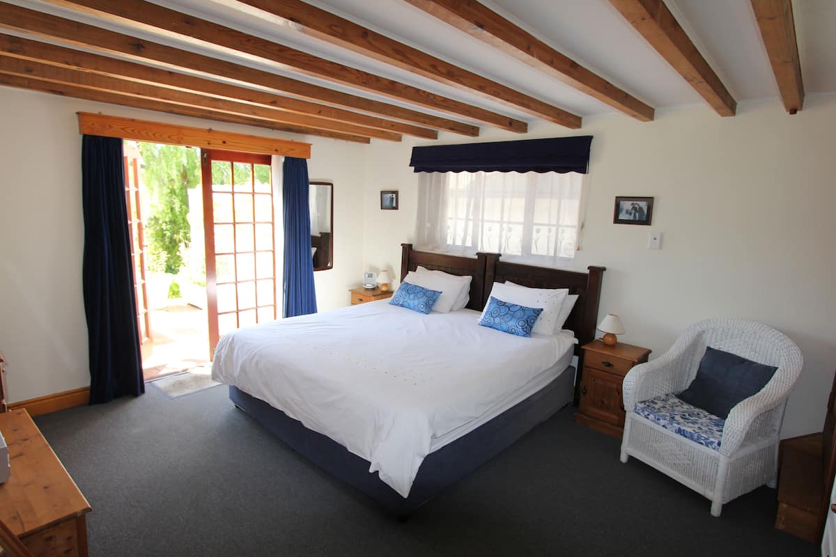 A bedroom with a large bed, a nightstand, a chair, and a window with curtains.
