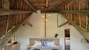Un dormitorio con cama, mesitas de noche, cómoda de madera, cabecera y techo con vigas a la vista.